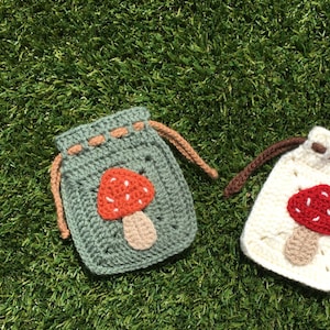 May include: Two crocheted drawstring bags with mushroom designs. One bag is green with a red and white mushroom, the other is white with a red and white mushroom.
