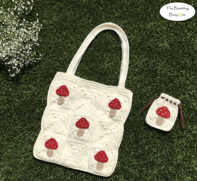 May include: White crocheted tote bag with red mushroom appliques. The bag has a small matching pouch with a red mushroom applique. The text "The Bumbling Busy Bee" is in the top right corner of the image.