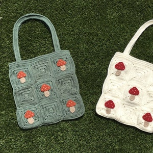 May include: Two crocheted tote bags with mushroom designs. One bag is green with red mushrooms and the other is white with red mushrooms.