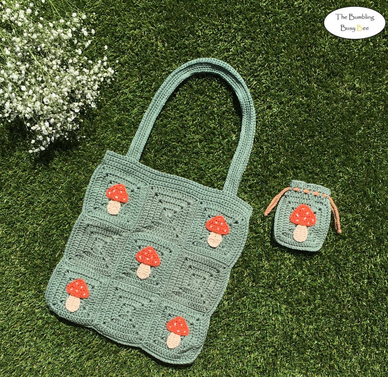 May include: A green crocheted tote bag with mushroom appliques. The bag has a small matching pouch with a mushroom applique. The text "The Bumbling Busy Bee" is visible in the top right corner of the image.