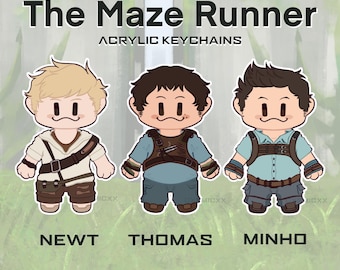 May include: Acrylic keychains featuring cartoon illustrations of Newt, Thomas, and Minho from "The Maze Runner." Each character is depicted in their signature outfits, with the names of the characters displayed below them. The background is a blurred green and white.
