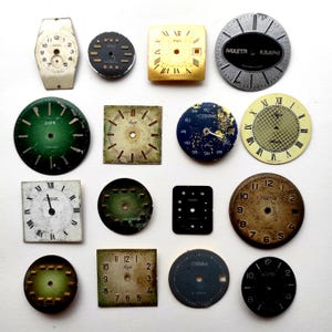 Op de afbeelding: Een verzameling van zestien vintage horlogewijzerplaten in verschillende vormen, kleuren en maten. Het assortiment bevat ronde en vierkante wijzerplaten met Arabische en Romeinse cijfers, Cyrillische tekst en verweerde texturen in groen, zwart, goud en wit.