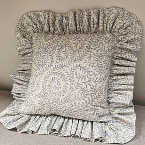 Könnte beinhalten: Ein quadratisches Kissen mit cremefarbenem Hintergrund und blauem Blättermuster. Es hat einen gerüschten Rand im gleichen Muster. Dieses dekorative Kissen ist wahrscheinlich für ein Bett oder Sofa gedacht.