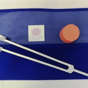 May include: A blue velvet pouch with a silver tuning fork and a red round mallet. The pouch has a small white label with a flower design and the text "ArtNam". The mallet has the number "18" printed on it.
