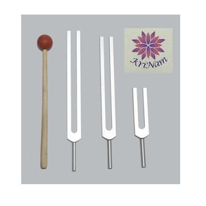 May include: A collection of tuning forks and a mallet for sound healing. The mallet has a wooden handle and a red ball head. Three silver tuning forks of varying sizes are displayed, along with a card with a floral design and the text "Kri Nam".