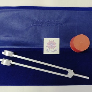 May include: A silver tuning fork with two adjustable weights, a red rubber mallet, and a blue velvet pouch with the text "KrizNam" printed on a sticker. The mallet has the number "18" printed on it.