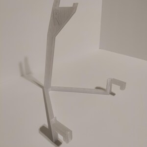 May include: A white plastic stand with three legs and a curved top. The stand is designed to hold a small object, such as a phone or a tablet.