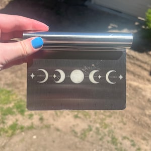 May include: A stainless steel pastry scraper with a moon and star design. The scraper has a ruler on the bottom with markings from 1 to 5.