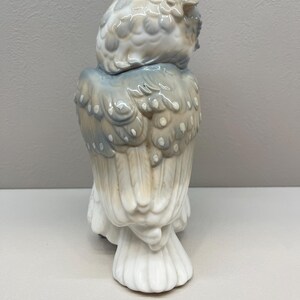 K&ouml;nnte beinhalten: Eine Eulenfigur aus Porzellan mit gl&auml;nzender Oberfl&auml;che in einer Farbpalette aus sanftem Grau, ged&auml;mpftem Blau und Cremewei&szlig;. Die Eule ist von hinten dargestellt und zeigt detaillierte Federstrukturen sowie geschichtete Fl&uuml;gelmuster.