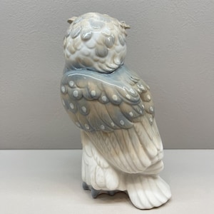 K&ouml;nnte beinhalten: Eine Eulenfigur aus Porzellan in einer sanften Farbpalette aus ged&auml;mpftem Blau, Beige und Wei&szlig;. Die Eule ist im Seitenprofil dargestellt und zeigt detaillierte Federstrukturen, kleine wei&szlig;e Punkte auf den Fl&uuml;geln und eine glatte Oberfl&auml;che.
