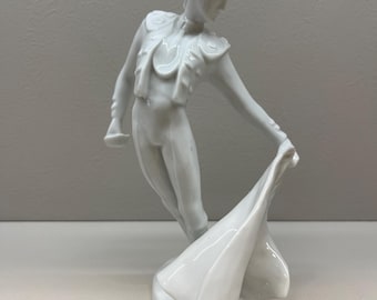 Pode incluir: Figurinha de porcelana branca de um toureiro com um traje tradicional, segurando uma capa na mão direita.