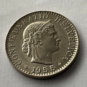 May include: A silver coin with the inscription "CONFEDERATIO HELVETICA" and the year "1955" around the edge. The center of the coin features a woman's profile with a crown and the word "LIBERTAS" above her head.