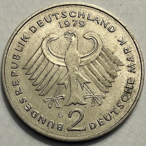 May include: A silver 2 Deutsche Mark coin from 1979. The coin features an eagle with outstretched wings, the words "BUNDESREPUBLIK DEUTSCHLAND" and "2 DEUTSCHE MARK" are inscribed around the edge. The year "1979" is also visible.