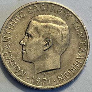 Op de afbeelding: Een zilveren Griekse munt met het profiel van koning Constantijn II en de tekst "ΒΑΣΙΛΕΥΣ ΚΩΝΣΤΑΝΤΙΝΟΣ" rond de rand. De munt heeft ook het jaar "1971" en de Griekse letter "S" onderaan.