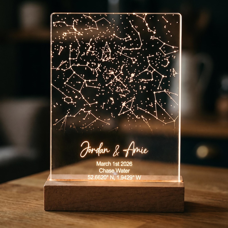 Puede incluir: Una luz nocturna rectangular de acr&iacute;lico con un dise&ntilde;o de mapa estelar iluminado. La base es de madera. El texto dice: Jordan & Amie, March 1st 2026, Chase Water, 52.6620 N, 1.9429 W. La l&aacute;mpara emite un brillo c&aacute;lido y suave.