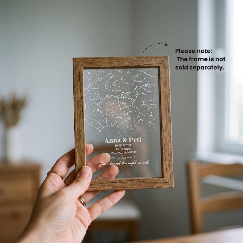 Puede incluir: Un marco de madera rectangular que contiene una l&aacute;mina acr&iacute;lica transparente impresa con un mapa de constelaciones blancas. El texto dice Anna & Peti, JUN | 25 | 2024, Margit Sziget, 47.5194972, 19.0459589, y Stars danced the night we met.