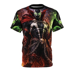 May include: Black t-shirt featuring a detailed graphic of a comic book character with a white emblem, chains, and a red cape. The character has glowing green eyes and is set against a fiery background with green orbs.