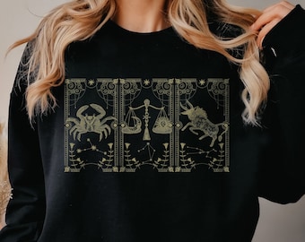 Könnte beinhalten: Schwarzes Sweatshirt mit einem goldenen Grafikdruck von Sternzeichen. Die Zeichen sind Krebs, Waage und Stier.