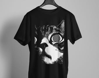 May include: A black short-sleeved t-shirt featuring a high-contrast white graphic print of a cat face. The cat's eyes are depicted as swirling spiral patterns, and the illustration uses bold, etched-style lines to define the feline features.