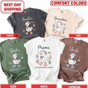 May include: Five short-sleeve t-shirts in pepper, ivory, moss, white, and espresso colors. Each shirt features a graphic of a white goose wearing a hat and boots, surrounded by flowers, with text including Auntie, Grandma, Dada, Mama, or Uncle.