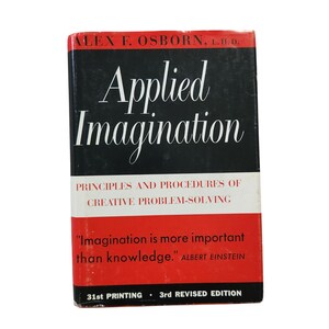 May include: A vintage book titled "Applied Imagination" by Alex F. Osborn. The cover is black with white text, including the title in a cursive font. The bottom section is red with a quote by Albert Einstein. The book is a 3rd revised edition.