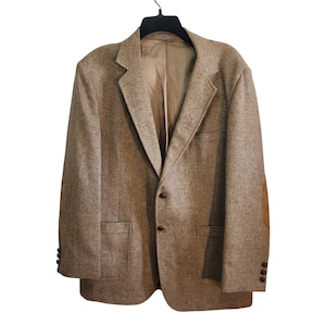 May include: A tan tweed blazer with brown elbow patches and buttons. The jacket has a notched lapel, two front pockets, and a single-breasted closure. The blazer is hanging on a black hanger.