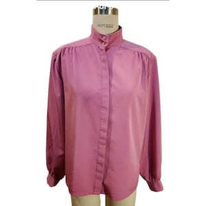 May include: A vintage mauve-colored blouse with a high collar and long sleeves. The blouse features a button-down front and gathered shoulders. The tag on the mannequin reads "DEPT 222".