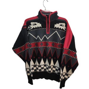 May include: A vintage black, red, and gray patterned sweater with a half-zip collar. The sweater features geometric and tribal designs, including diamond, zigzag, and checkerboard patterns. The sleeves and collar are accented with red.