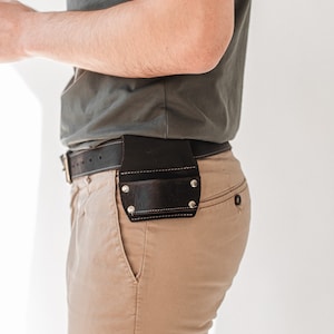 May include: A person wearing a grey t-shirt and khaki trousers with a brown leather belt and a tool holder attached to the belt.