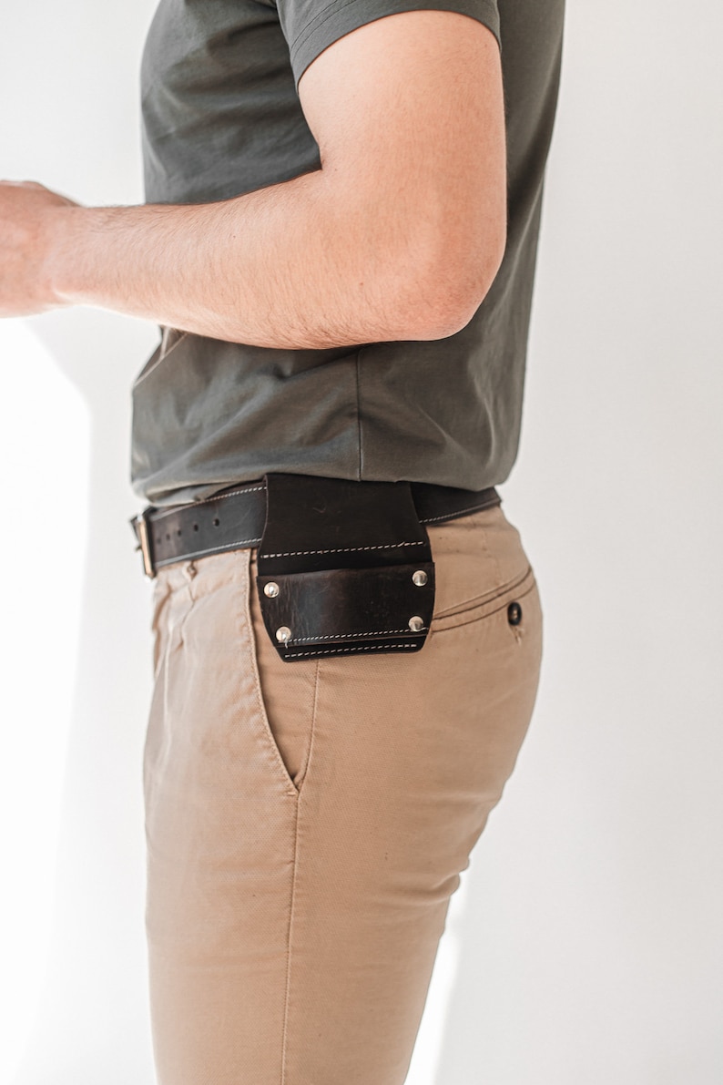 May include: A person wearing a grey t-shirt and khaki trousers with a brown leather belt and a tool holder attached to the belt.