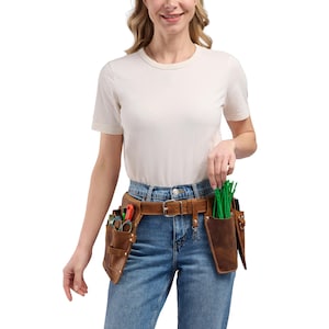 May include: A brown leather tool belt featuring multiple pockets and pouches, secured with a metal buckle. The belt is worn around the waist and contains various small tools and green pipe cleaners stored within the leather compartments.