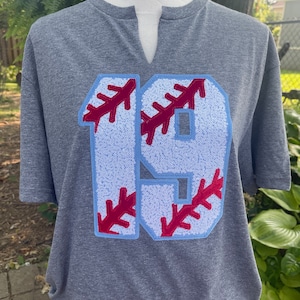 May include: A gray t-shirt with a blue and red baseball-themed number 19 sewn on the front.