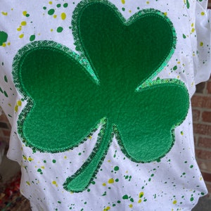 May include: White t-shirt with green and yellow paint splatters and a large green shamrock with sequins.