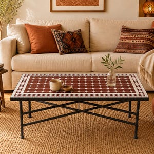 May include: A rectangular coffee table with a black metal frame and a tiled top featuring a repeating pattern of dark red squares with white circular accents and a white diamond border. A ceramic mug and a small bowl sit on the table surface.