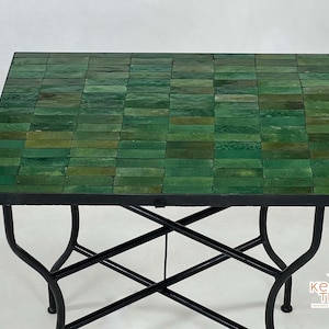 Pode incluir: Uma mesa com tampo de azulejos verdes e base de metal preto. A mesa tem um design em forma de cruz na base.