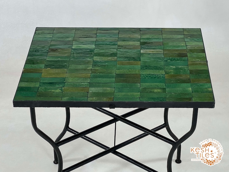 Pode incluir: Uma mesa com tampo de azulejos verdes e base de metal preto. A mesa tem um design em forma de cruz na base.