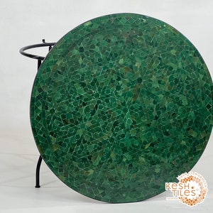 Może przedstawiać: Okrągły blat stołu z zielonej mozaiki z czarnym metalowym stelażem. Blat stołu wykonany jest z małych zielonych płytek ułożonych w geometryczny wzór. Stelaż jest prosty i ma okrągłą podstawę.