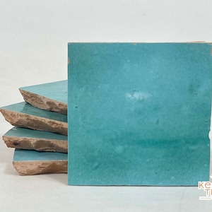 May include: Stack of four teal blue ceramic tiles with rough edges. The tiles are handmade and have a rustic, vintage look.