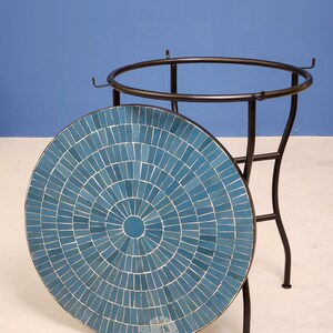 May include: A round mosaic tile table with a black metal frame. The tabletop is a mosaic of blue tiles arranged in a radial pattern. The table is approximately 61 cm in diameter and 71 cm tall.