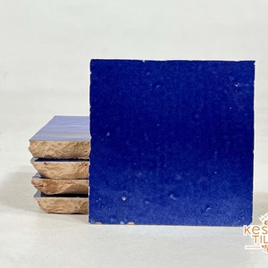 May include: Stack of four blue ceramic tiles with a rough texture. The tiles are arranged in a staggered pattern, with the top tile slightly offset from the others. The tiles are a deep, rich blue color, and the texture gives them a slightly uneven surface.