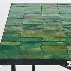 Pode incluir: Uma mesa com tampo de azulejos verdes e moldura de metal preto. Os azulejos est&atilde;o dispostos em forma de grade.