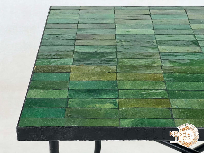 Pode incluir: Uma mesa com tampo de azulejos verdes e moldura de metal preto. Os azulejos est&atilde;o dispostos em forma de grade.