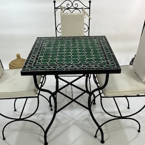May include: A black wrought iron patio set with a green mosaic tile table top and four chairs. Each chair has a white cushion.