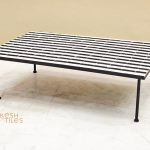 May include: Rectangular coffee table with a black and white striped tile top. The table has a black metal frame and legs. The table is approximately 48 inches long and 24 inches wide.