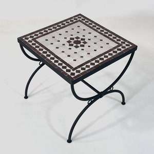 May include: A square, white and brown mosaic tile top table with a black metal frame. The table has a simple, elegant design and would be perfect for a patio or garden.