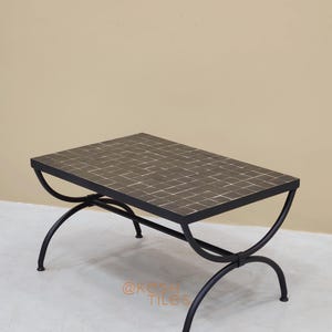 May include: Rectangular coffee table with a mosaic tile top and a black metal frame. The table's top is a mosaic of small, dark-colored tiles. The legs are curved, adding a unique design element. The table measures approximately 48 inches long and 24 inches wide.