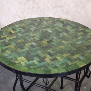 Könnte beinhalten: Runder Mosaiktisch mit grüner Fliesenplatte und schwarzem Metallrahmen. Die Tischplatte hat ein Muster aus rechteckigen Fliesen in Grüntönen. Der Tisch hat einen Durchmesser von ca. 76 cm.