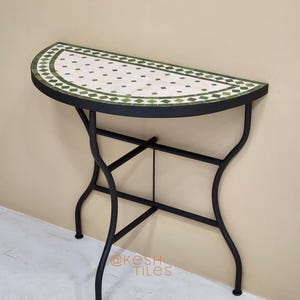 May include: A half-moon console table with a mosaic tile top. The tabletop features a white background with green diamond-shaped tiles and a green border. The black metal frame has curved legs. The text "@kesh TILES" is visible.