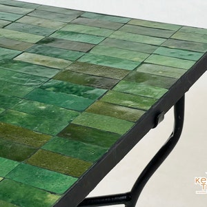 Pode incluir: Uma mesa com tampo de azulejos verdes e base de metal preto. Os azulejos est&atilde;o dispostos em forma de tijolo.