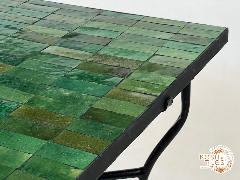 Pode incluir: Uma mesa com tampo de azulejos verdes e base de metal preto. Os azulejos est&atilde;o dispostos em forma de tijolo.
